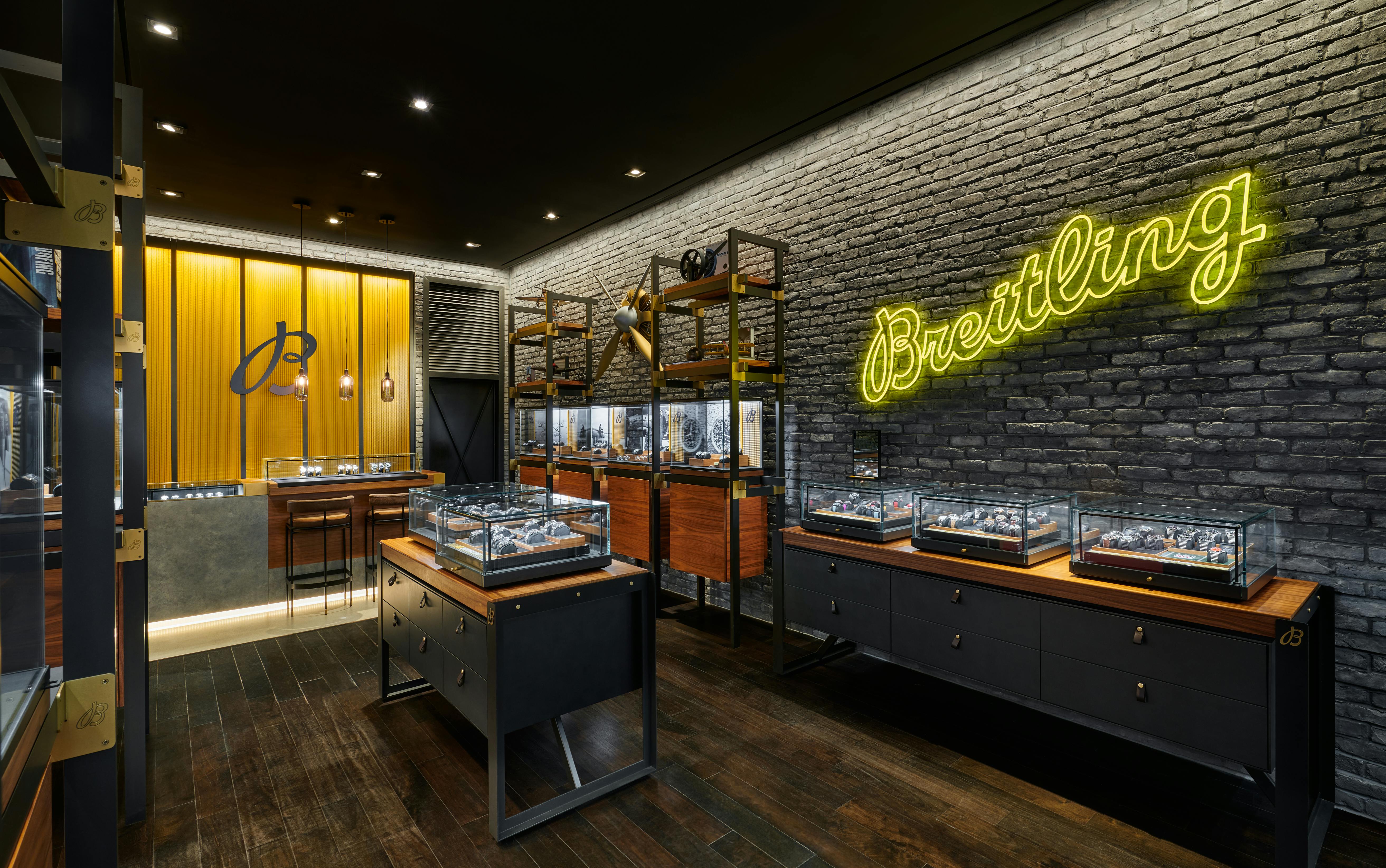 Luxury Breitling retail showroom with neon logo sign, glass display cases, and industrial stone wall design