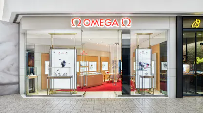 Exterior storefront of Omega boutique at The 1916 Company with illuminated logo and glass entrance