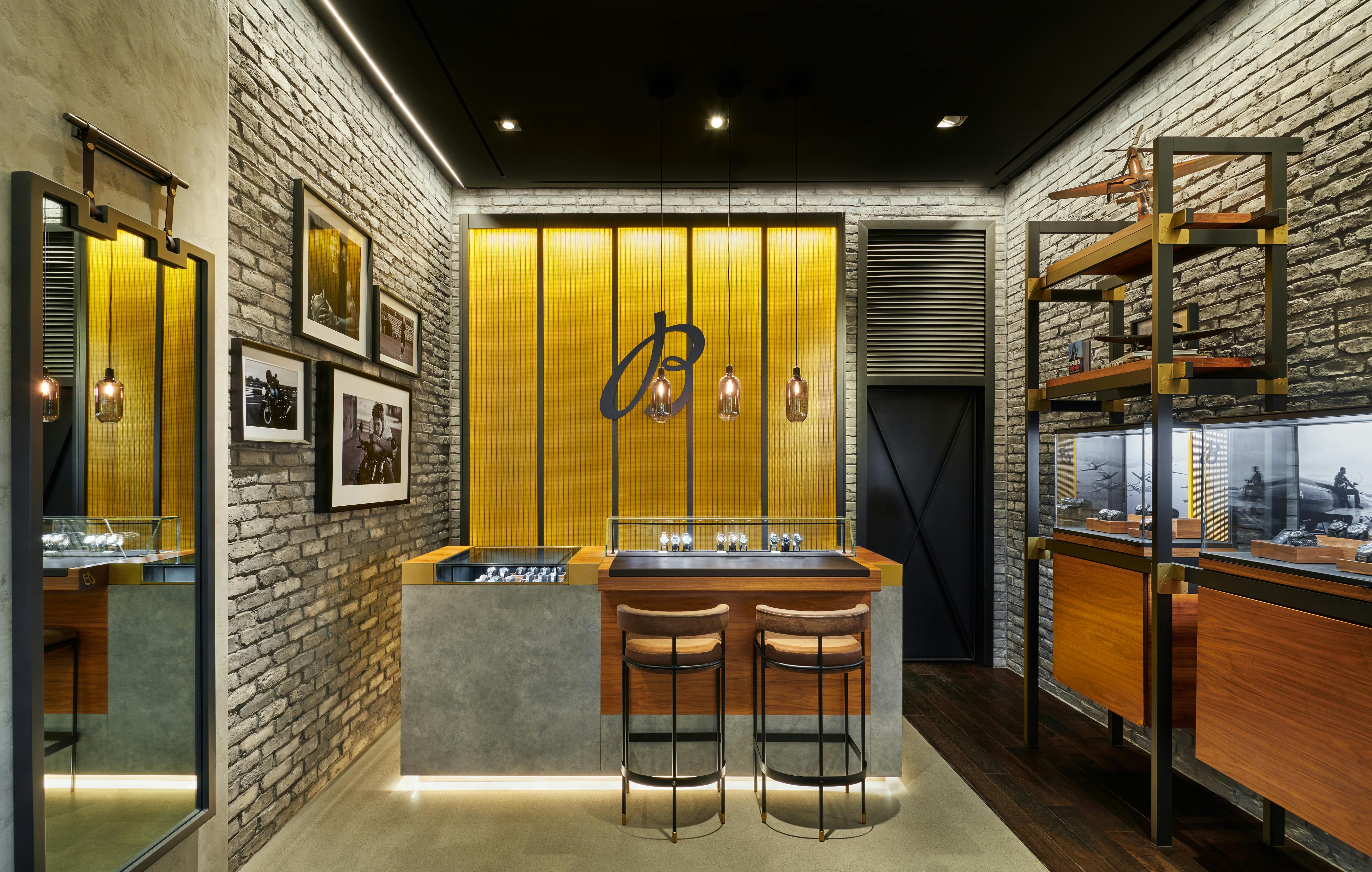 Interior of Breitling boutique featuring yellow backlit wall, stone accents, and watch display counter with leather stools