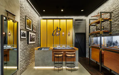 Interior of Breitling boutique featuring yellow backlit wall, stone accents, and watch display counter with leather stools