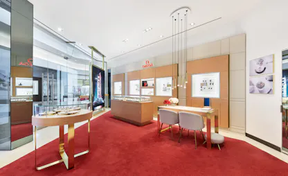 Omega retail interior with glass display tables, consultation seating area, and red carpet flooring