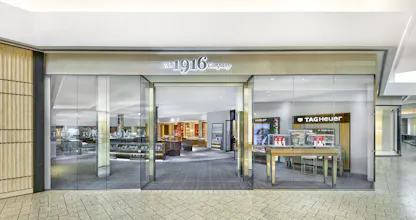 Front entrance of The 1916 Company Denver, with a glass storefront showing Hublot, TAG Heuer, and Cartier watch displays inside.