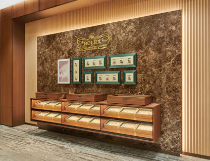 Rolex Certified Pre-Owned watch display wall with green-framed watch cases and illuminated wood display cases at The 1916 Company