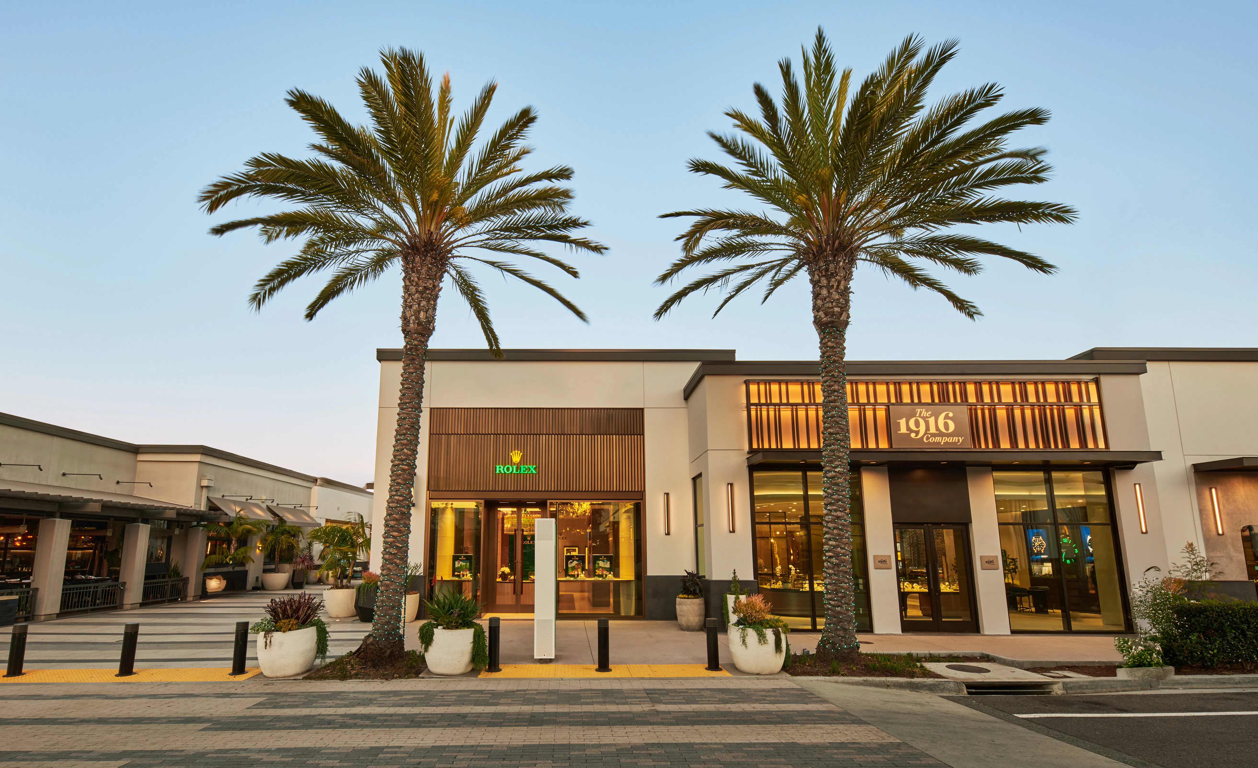 The 1916 Company and Rolex authorized dealer storefront exterior with palm tree-lined street at golden hour
