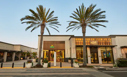 The 1916 Company and Rolex authorized dealer storefront exterior with palm tree-lined street at golden hour