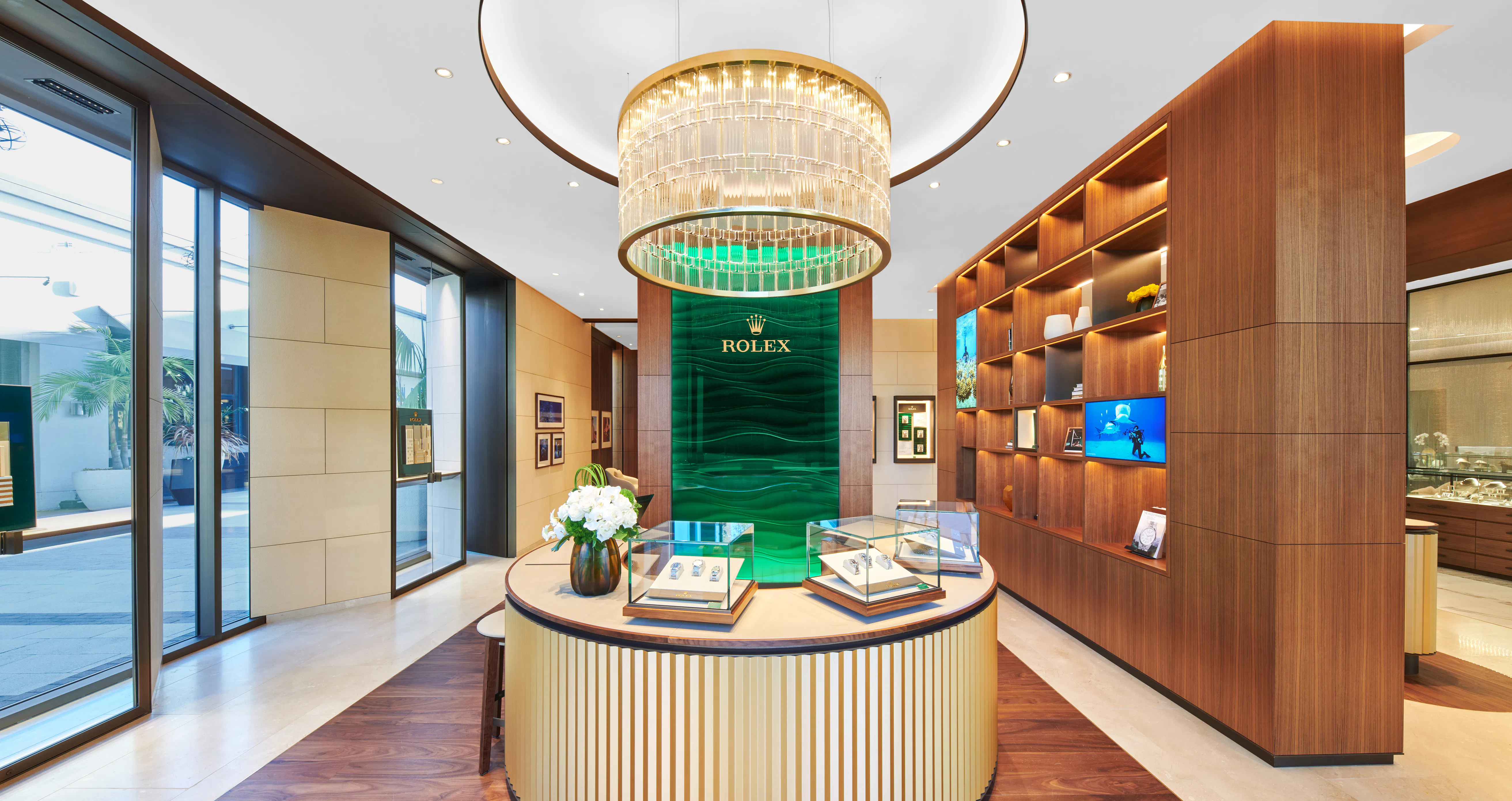Rolex authorized dealer showroom interior featuring circular watch display counter, crystal chandelier, and green marble brand column