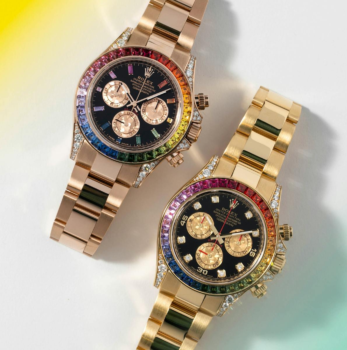A side-by-side photograph of the Rolex Rainbow Daytona watch in Everose and Yellow, comparing the colorful baguet gem indices of the Everose model.